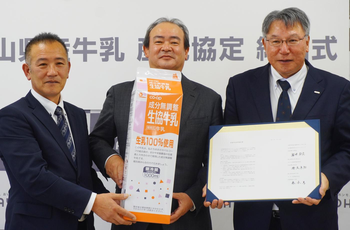 岡山市のオハヨー乳業本社で開かれた協定締結式。（左から）「生協牛乳」と協定書を持って写真撮影に応じる檜尾康知組合長、奥井和久理事長、藤本篤社長