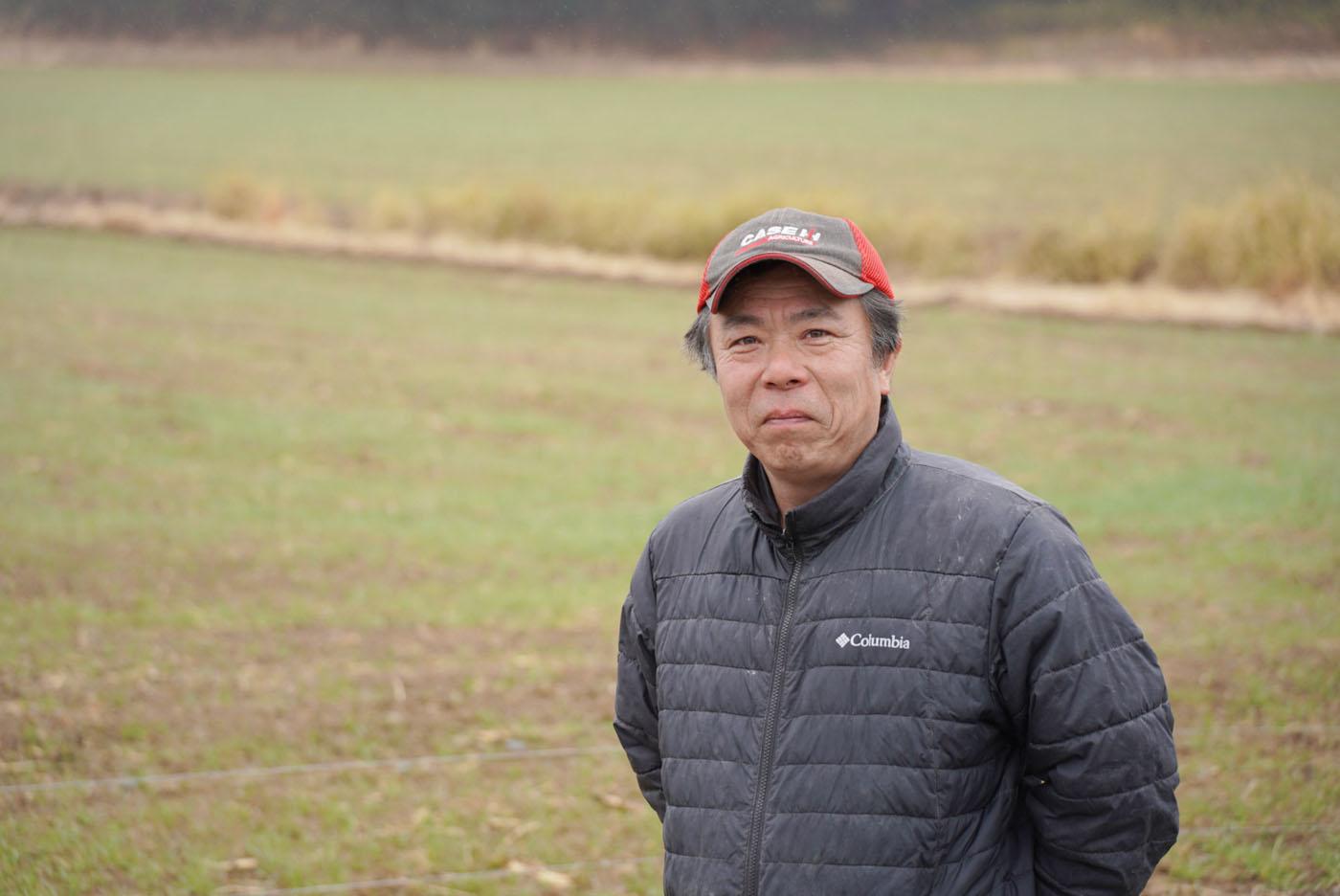 芽吹き始めた牧草の前に立つ相馬秀一さん